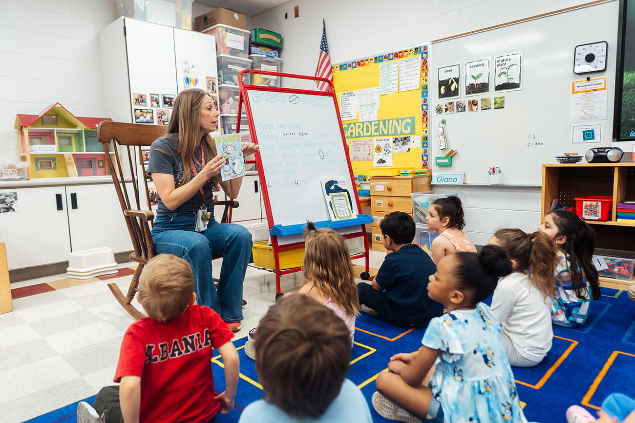Teacher sharing a book in front of children on a rug in a preschool classroom setting