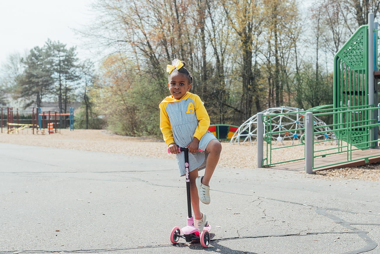 A young child riding a scooter in a playground setting