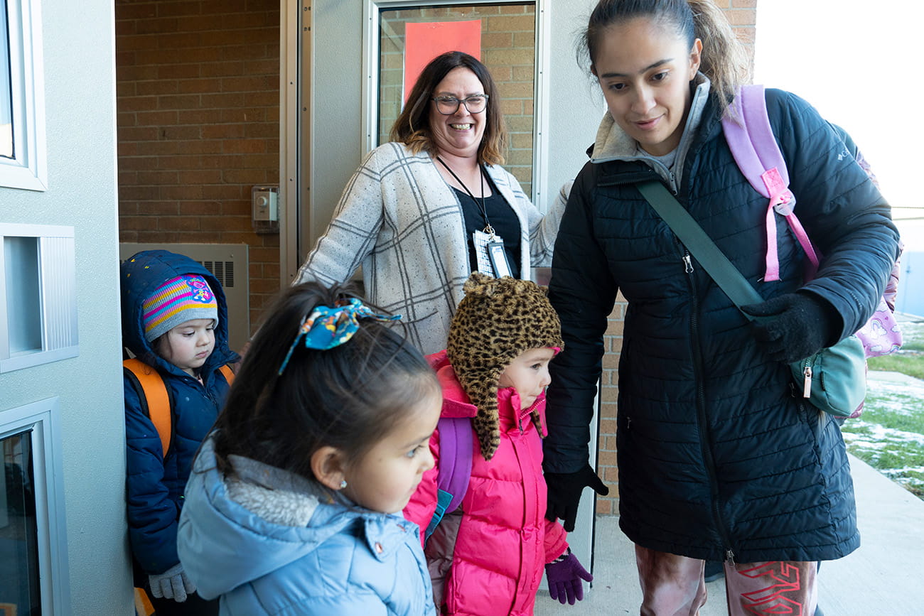 An adult picking up children from the door of a preschool classroom