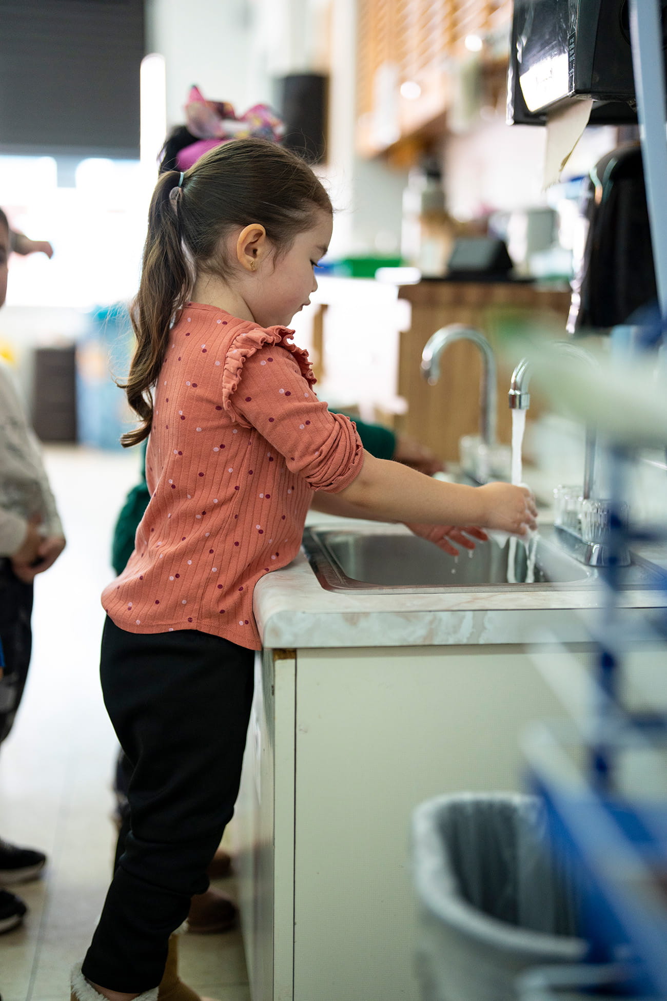 A young child washes her hands at a sink in a preschool classroom