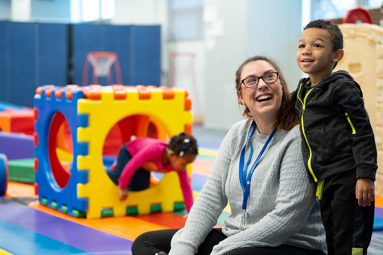 A teacher seated on the floor looking up a student standing next to her