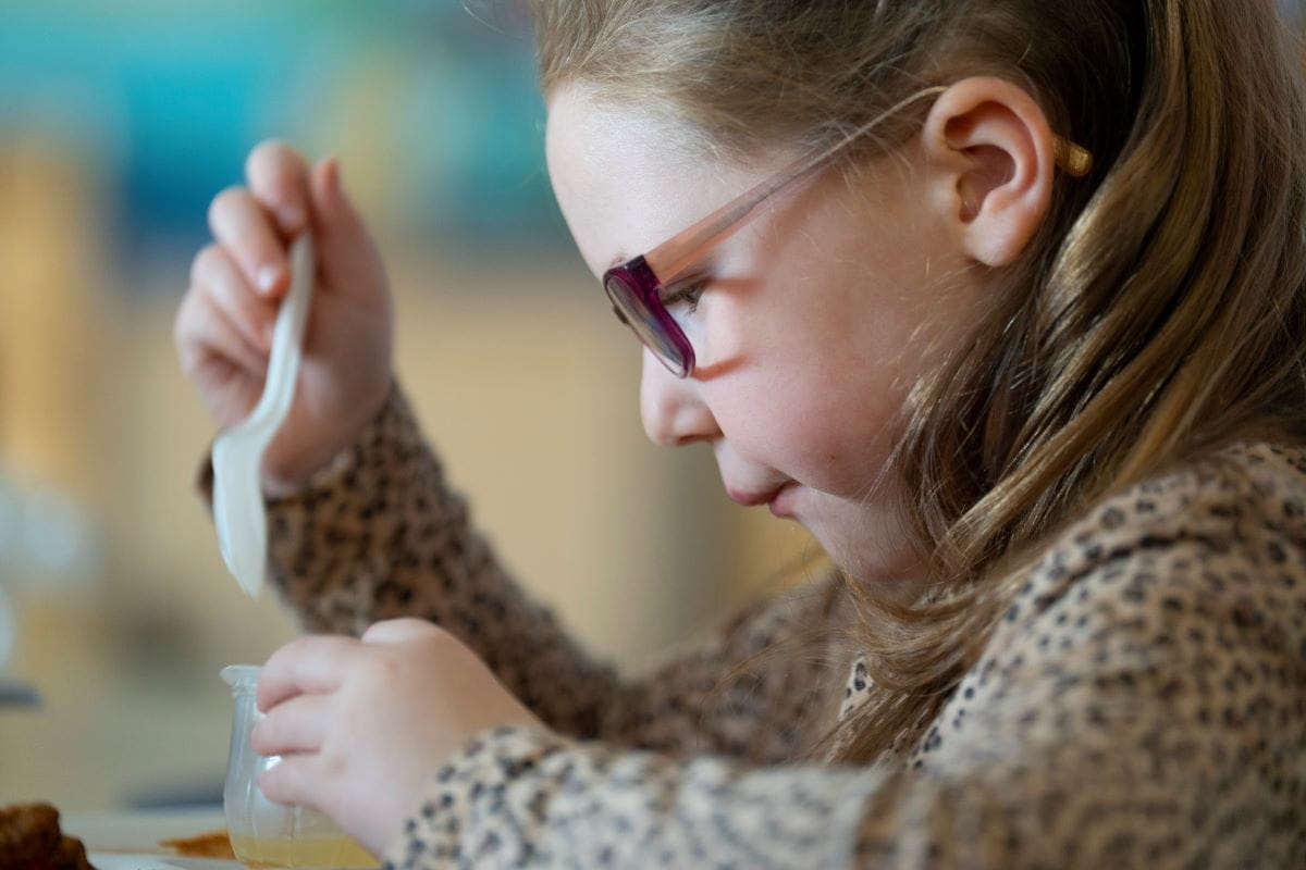 A close up of a young child with glasses eating a snack