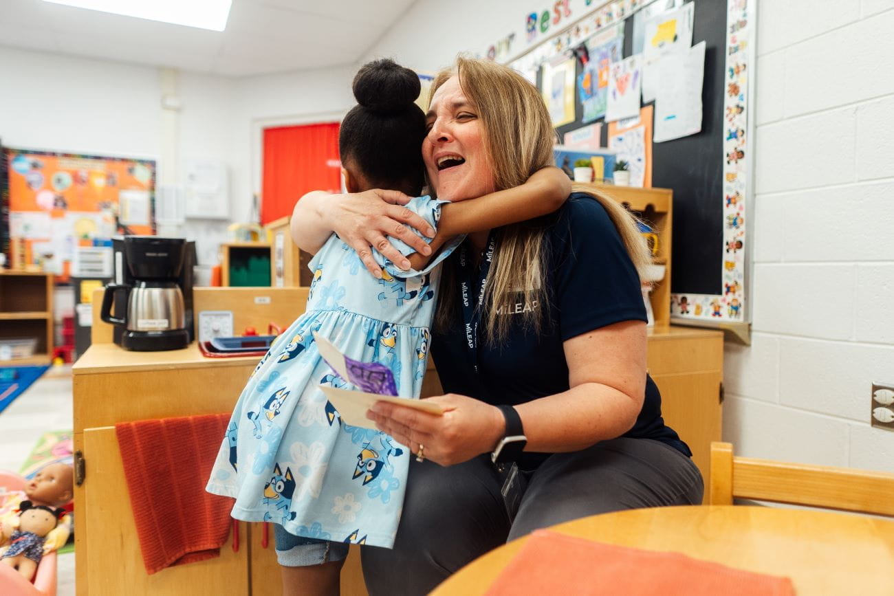 A young child hugging a preschool teacher in a classroom setting