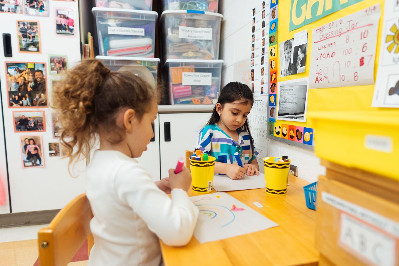 Two students seated at a desk in a preschool classroom