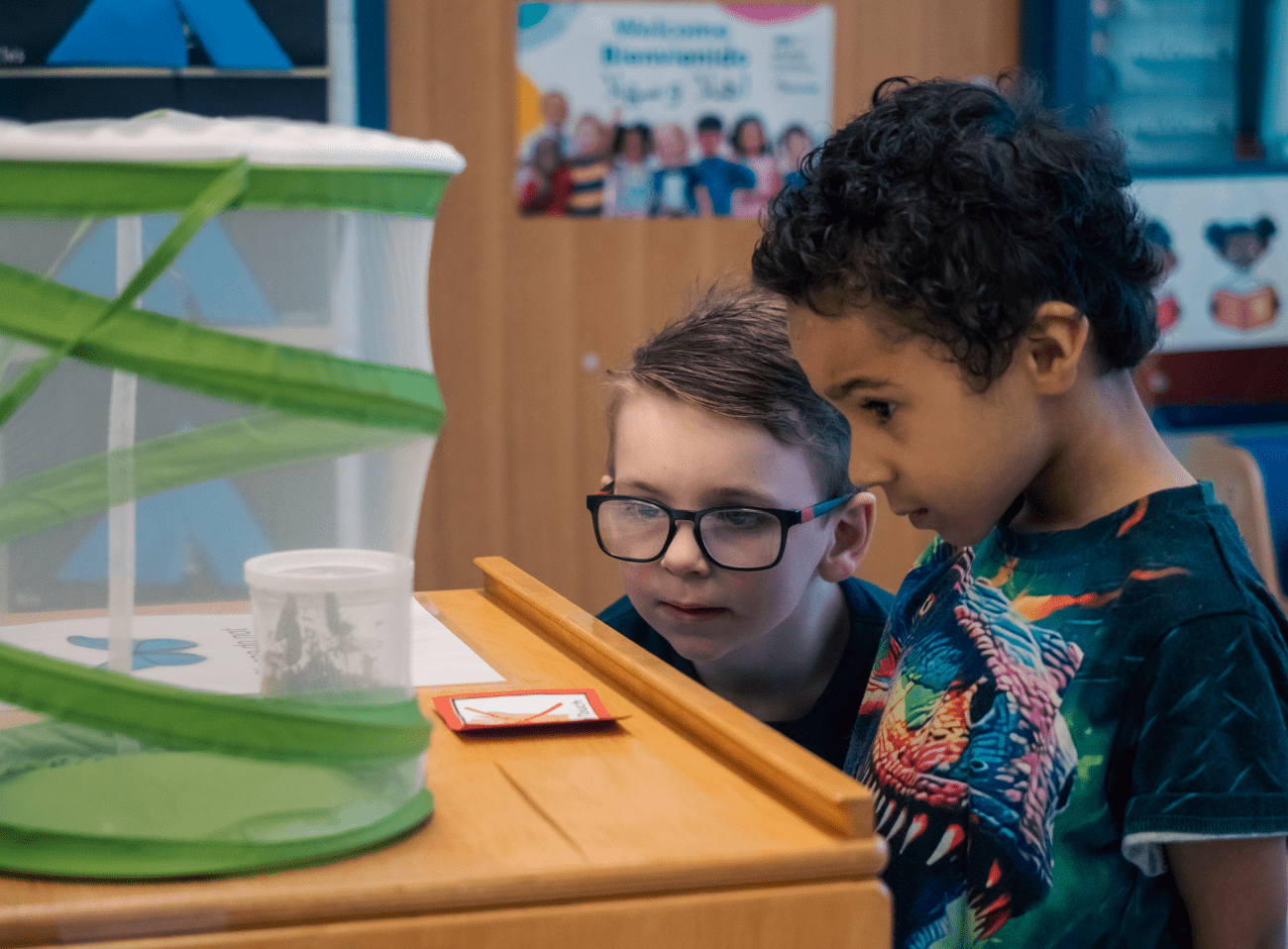 Two young children looking at items on a bookshelf in a preschool classroom