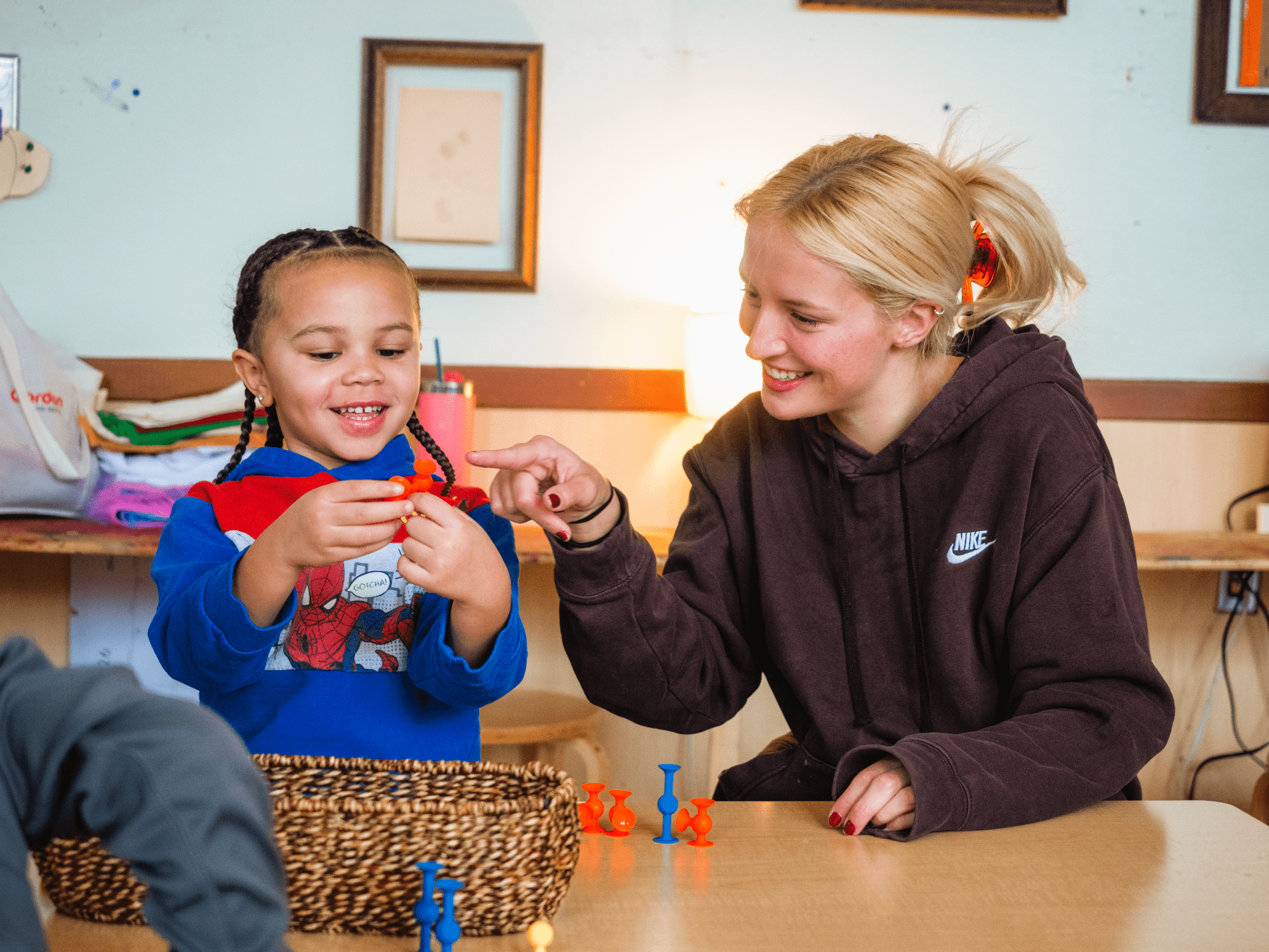Child and adult sitting together at a table and smiling while playing with toys