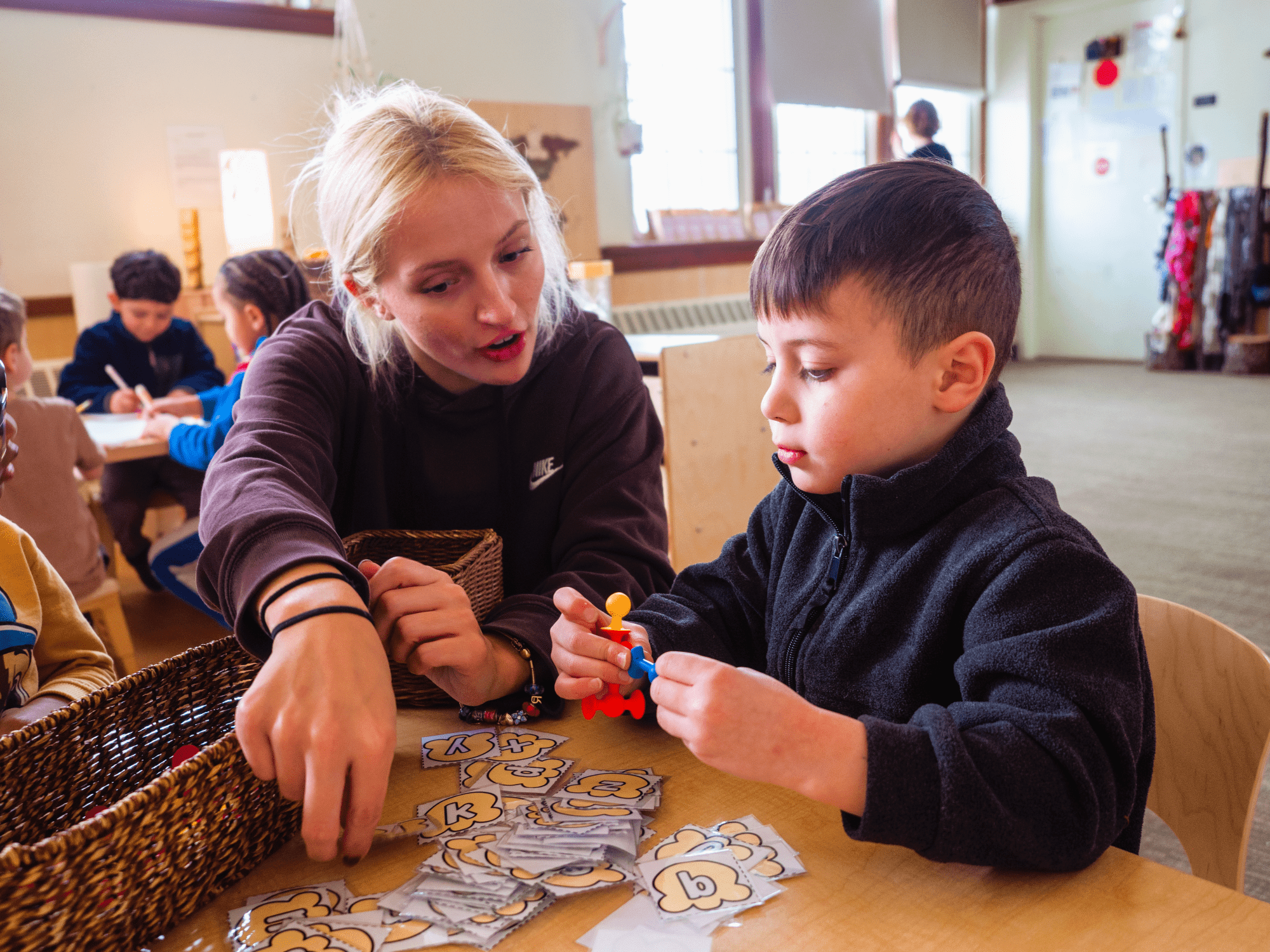 A teacher kneeling next to a child at a table reviewing alphabet flashcards