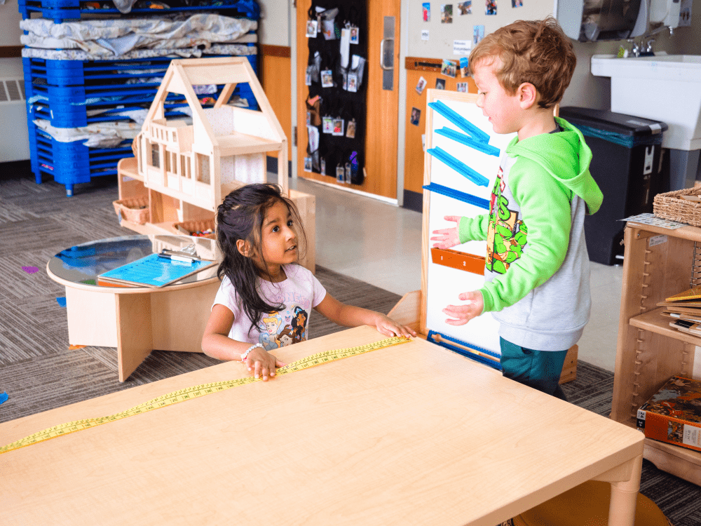 Two preschool students interacting at a table in a classroom