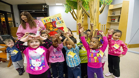 A group of children, with their teacher behind them, hold up a book.