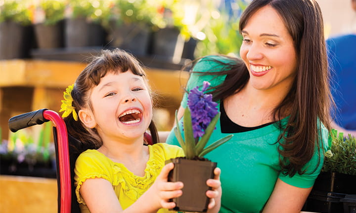 Smiling girl in wheelchair holding plant as mother kneels beside her