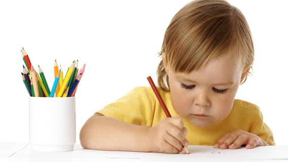 preschooler at table drawing on paper with colored pencil with a cup of colored pencils beside him