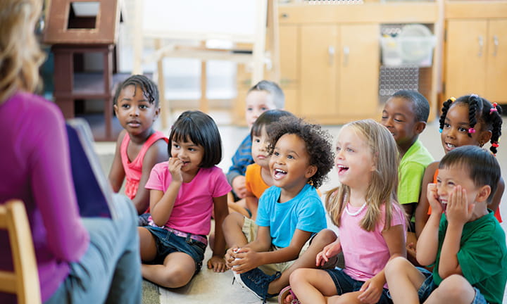 provider reading to group of smiling engaged children in classroom
