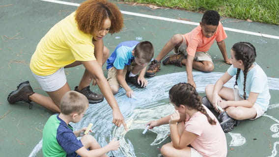 five school with teacher outside drawing on sidewalk with chalk