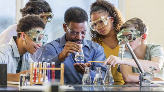 four school children in lab with teacher doing experiment