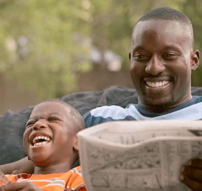 Adult and young child laughing together while reading a newspaper