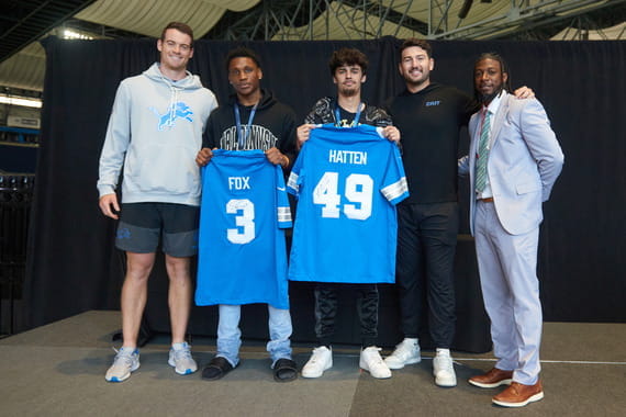 Students pose with Detroit Lions players Jack Fox and Hogan Hatten, alongside Derrick King, director of Upward Bound at Muskegon Community College and MI Kickoff MC, after winning a game of rock, paper, scissors.
