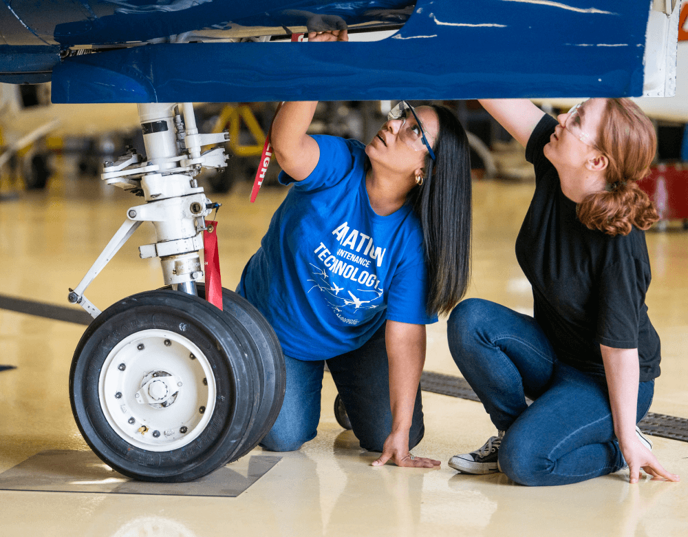 Two people looking underneath an airplane.