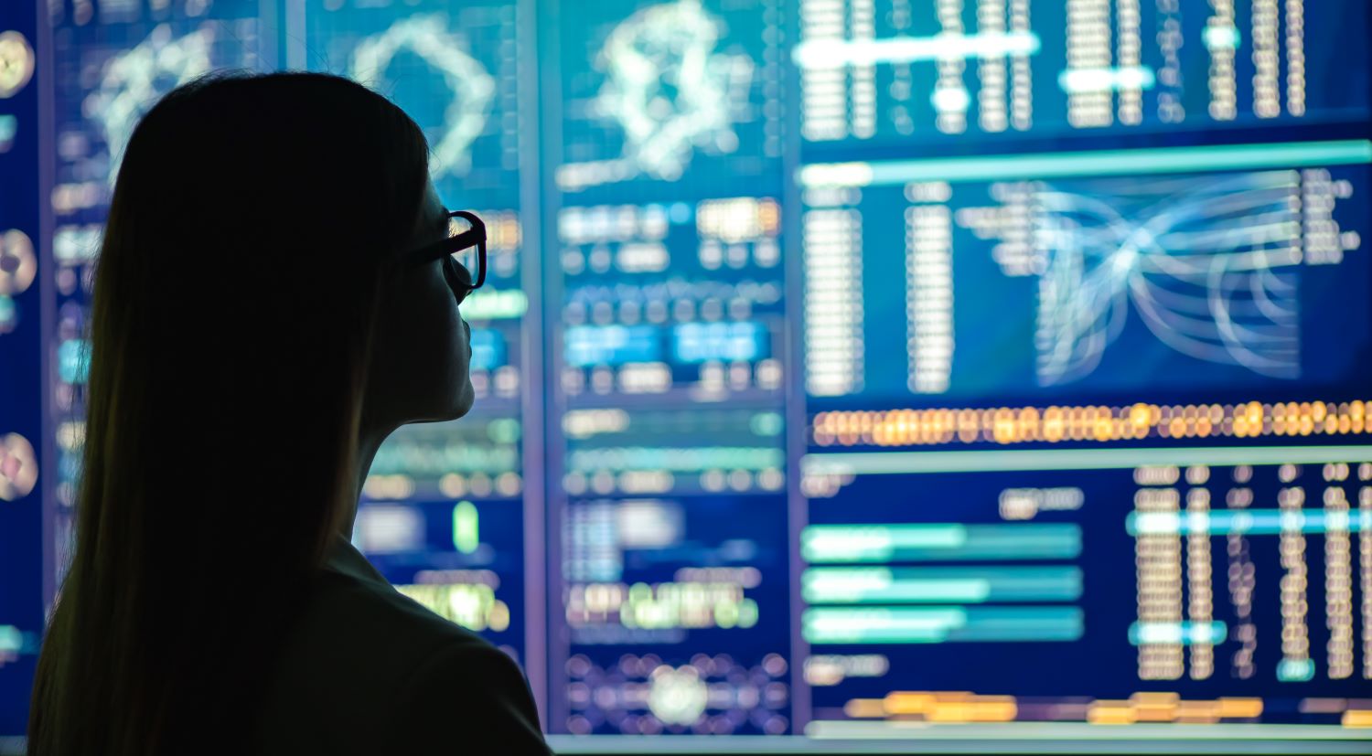 Silhouette of a woman looking at computer screens on the wall
