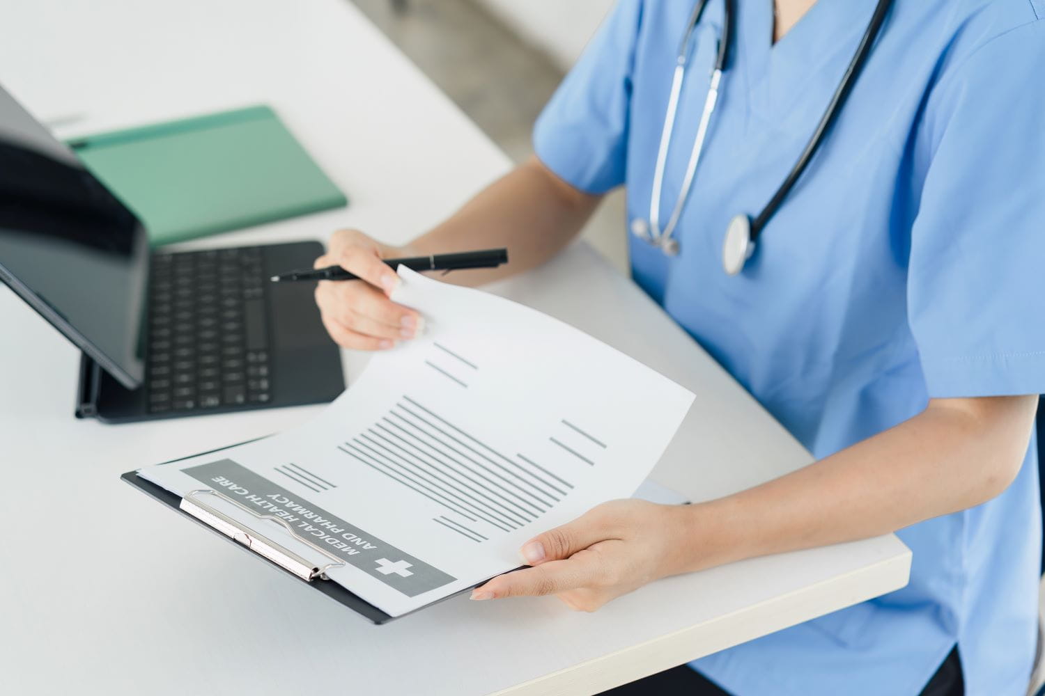 A close up of a healthcare worker's hands while sitting at a desk looking at a clipboard