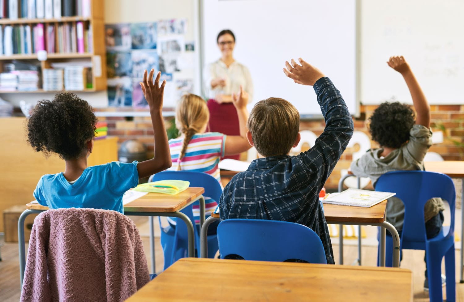 A teacher standing in front of a classroom with students raising their hands