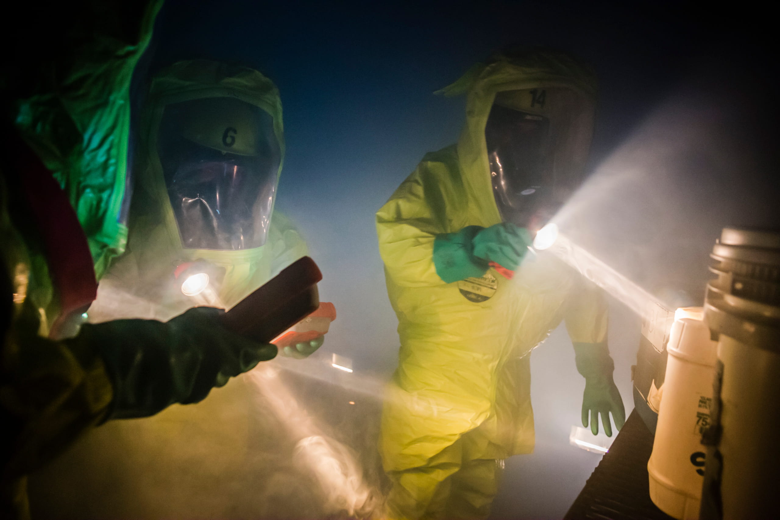 People in hazmat suites in a dark area with flashlights.