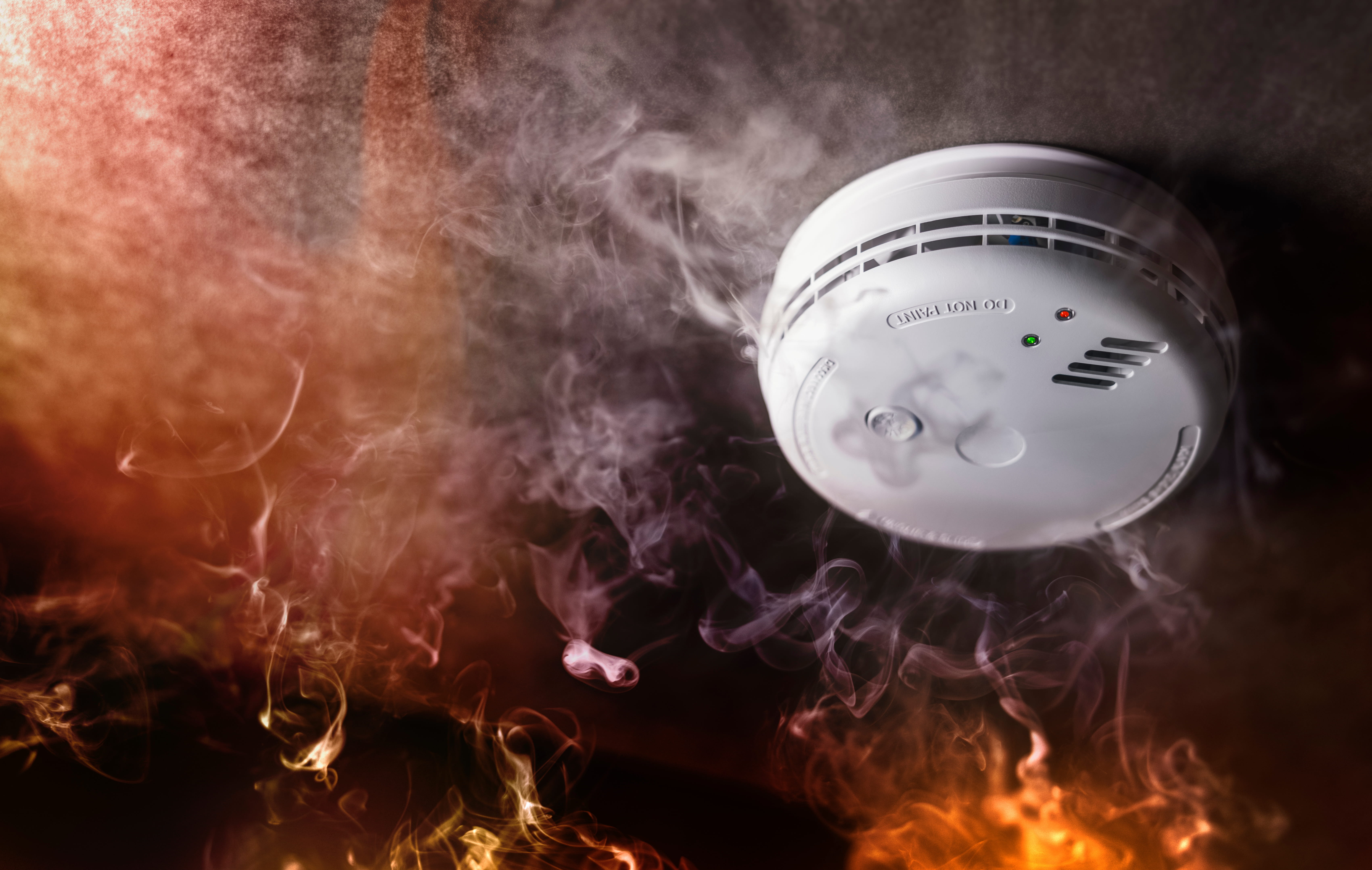 A smoke detector with smoke and flames around it