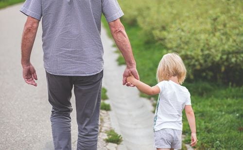 Grandfather holding hands with grandchild walking down a sidewalk