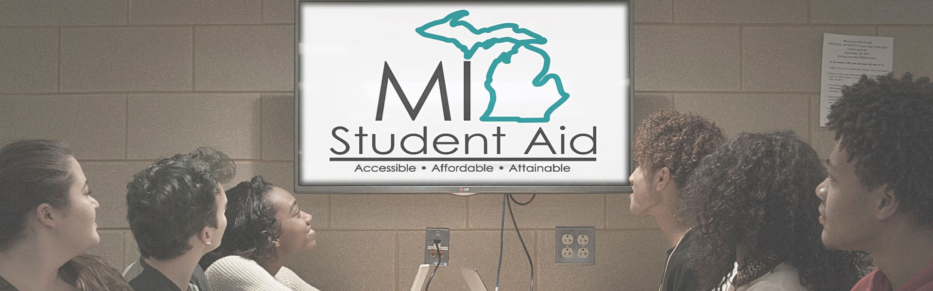Students looking at MI Student Aid logo on monitor.