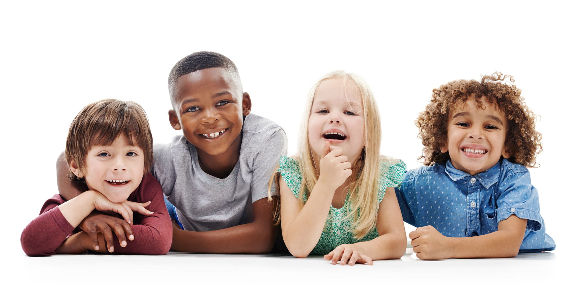 Four, diverse children laying on stomachs, smiling at camera