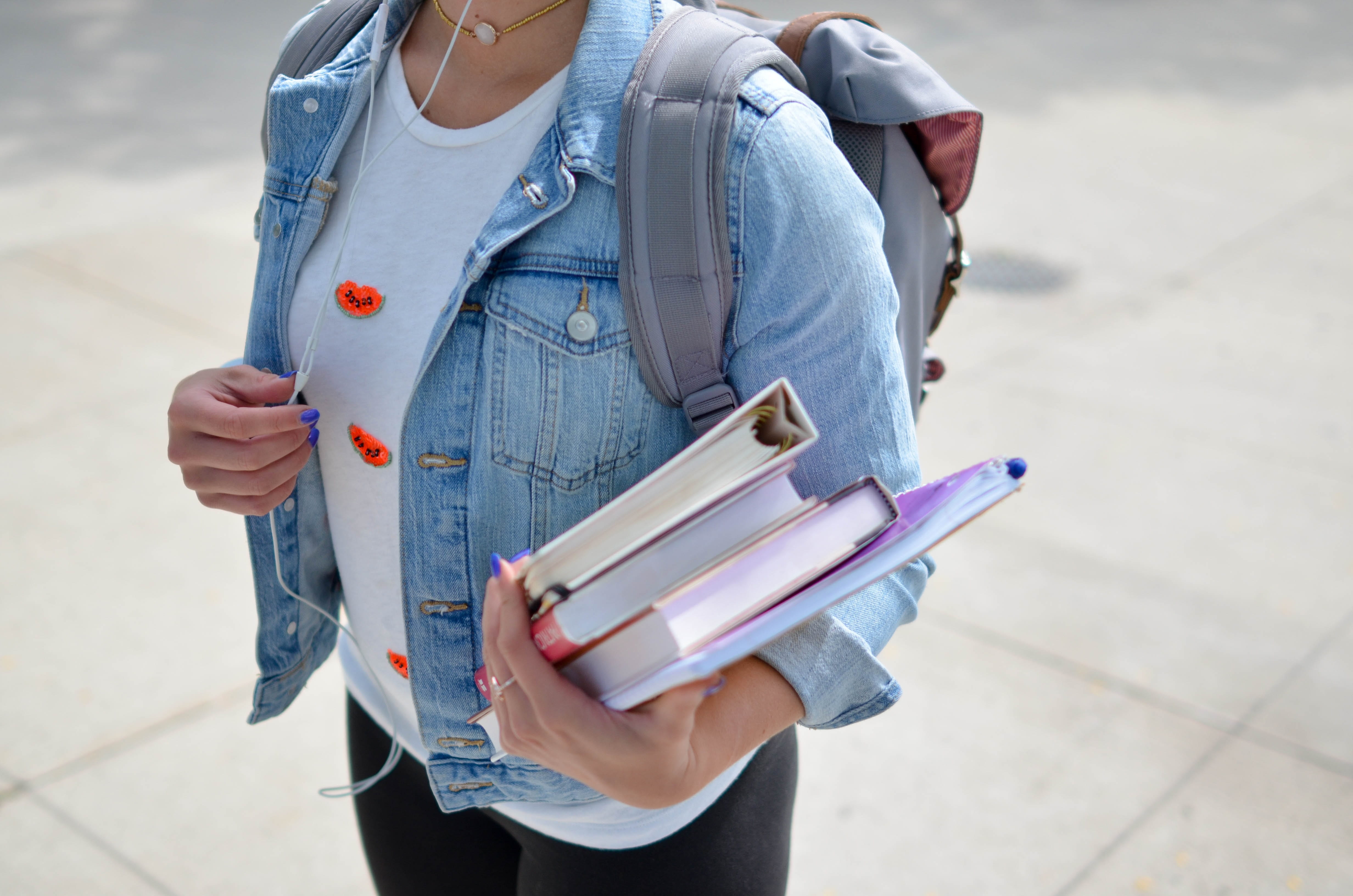 Someone holding books in their hand while wearing a backpack.
