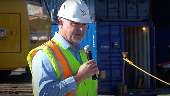 Bart Pickleman in Construction hat and safety vest at construction site speaking on a microphone