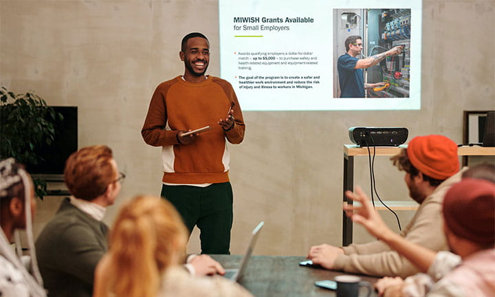 Man speaking in front of a group about MIWISH with presentation showing behind him