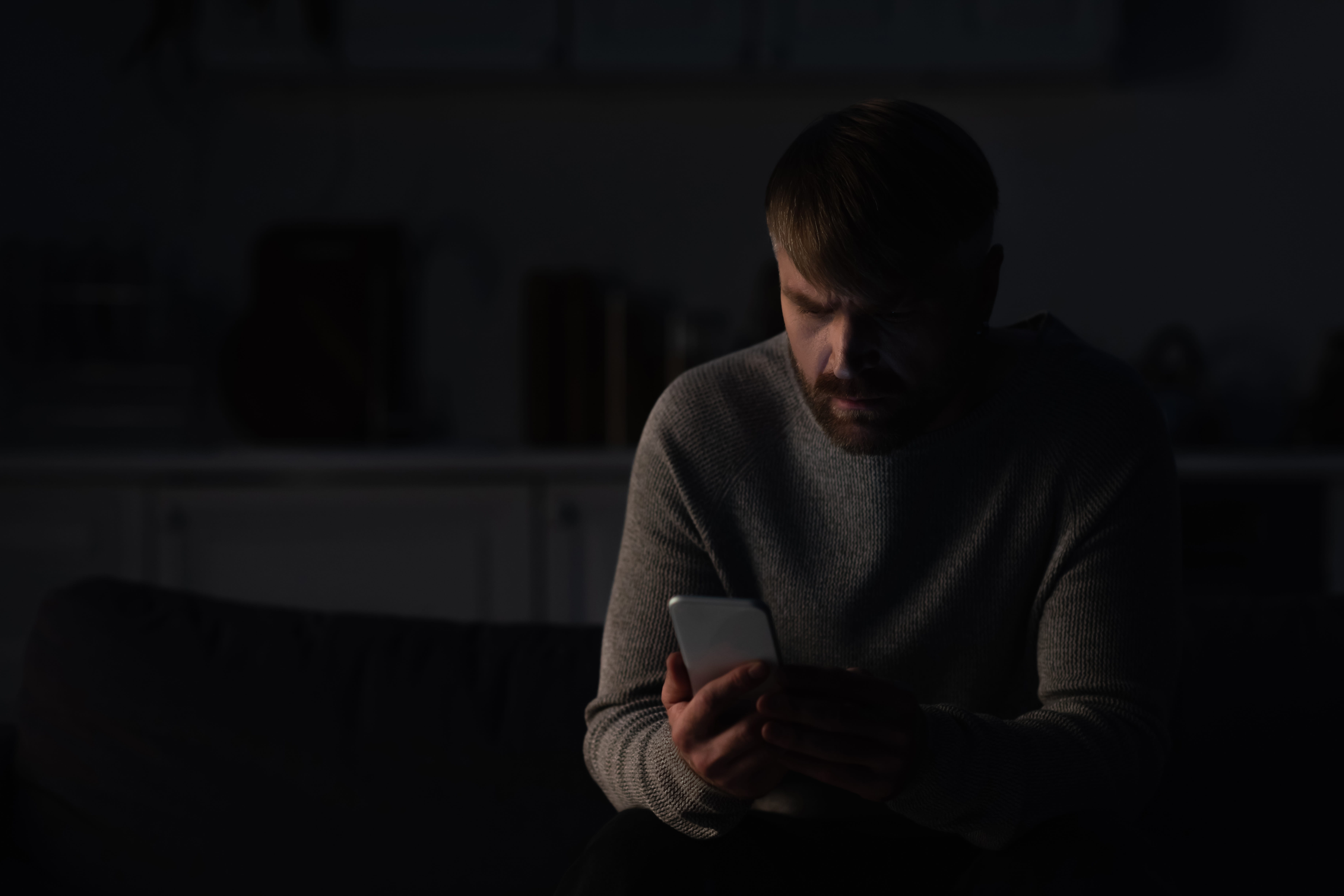 man sitting in dark kitchen and using mobile phone during energy blackout.
