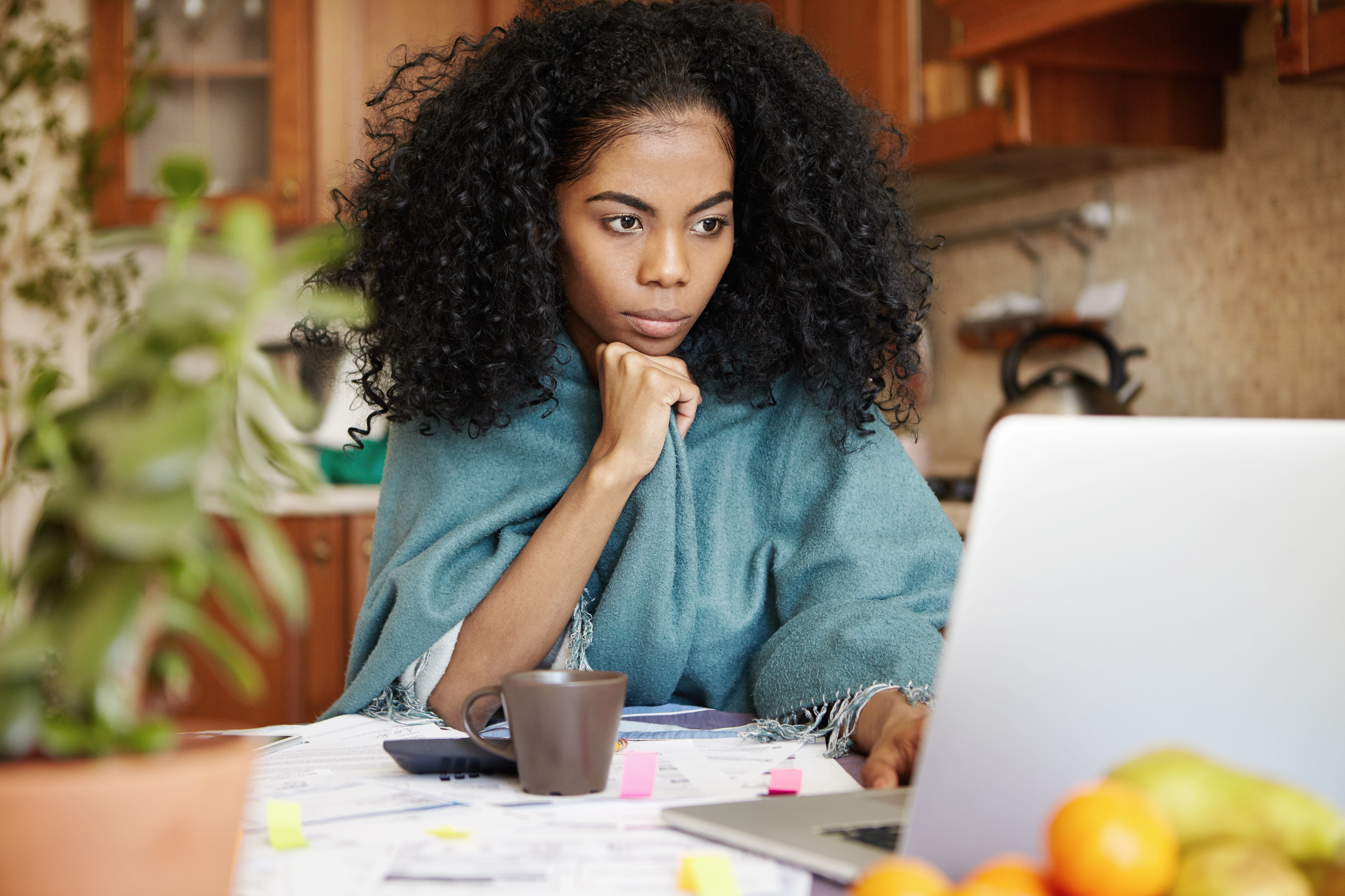 Woman sitting in front of laptop computer, looking at screen with serious and concentrated expression, having coffee while paying utility bills via Internet