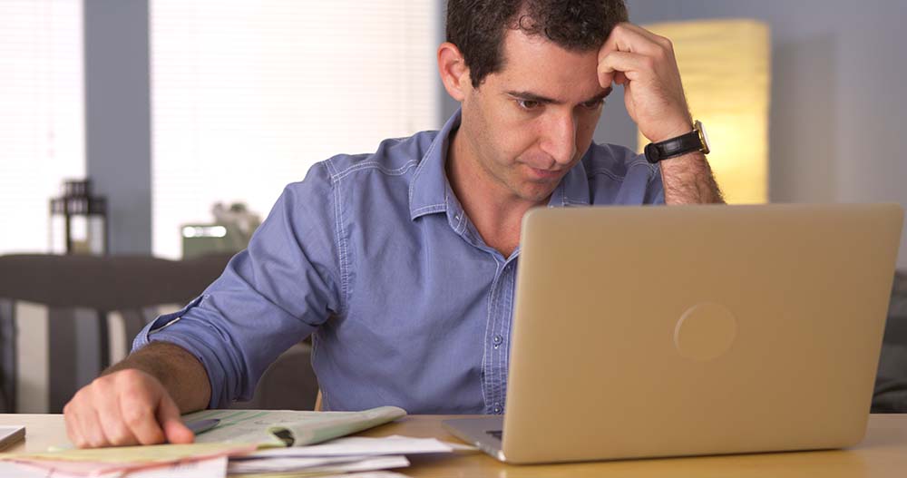 Frustrated man staring at computer while doing bills