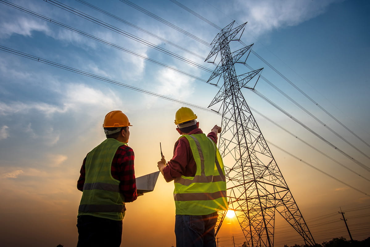 Picture of two electrical engineers checking electrical work using a computer standing at a power station to see the planning work at high voltage power lines.