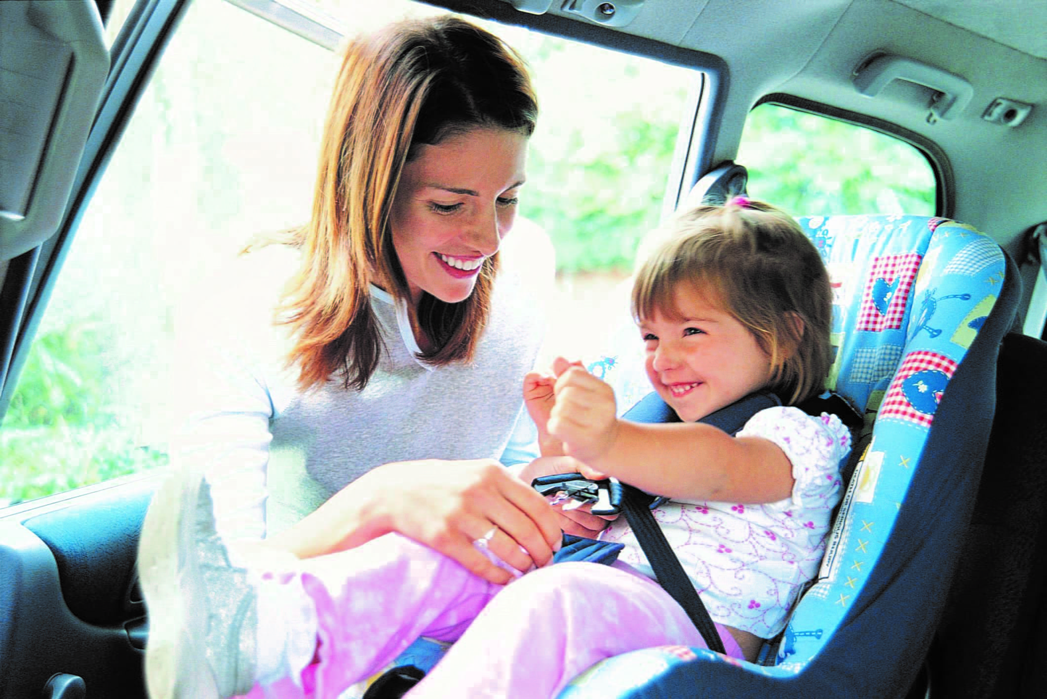 Woman buckling up child into a car seat