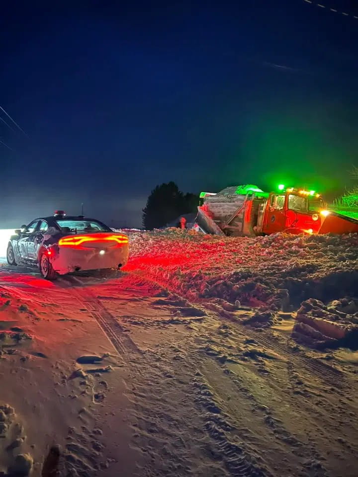 A Michigan State Police car on a snow-covered road next to a snow plow that is off the road in deep snow.