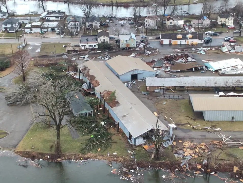 An aerial view of damaged buildings, trees, and debris after a tornado.