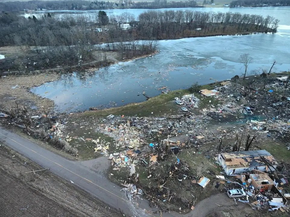An aerial view of damaged houses and trees next to a lake after a tornado.