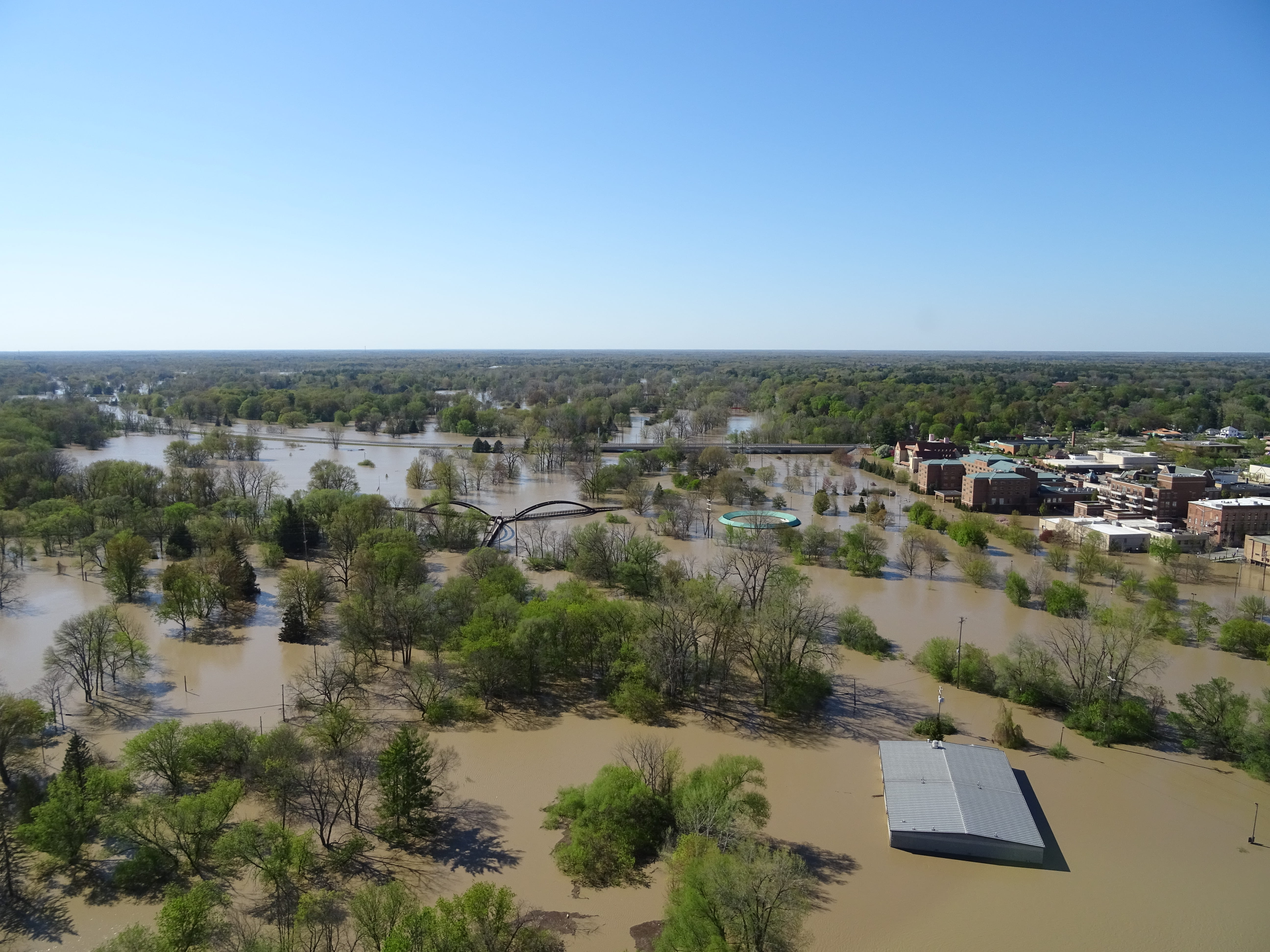 An aerial view of trees and buildings surrounded by flood water. 