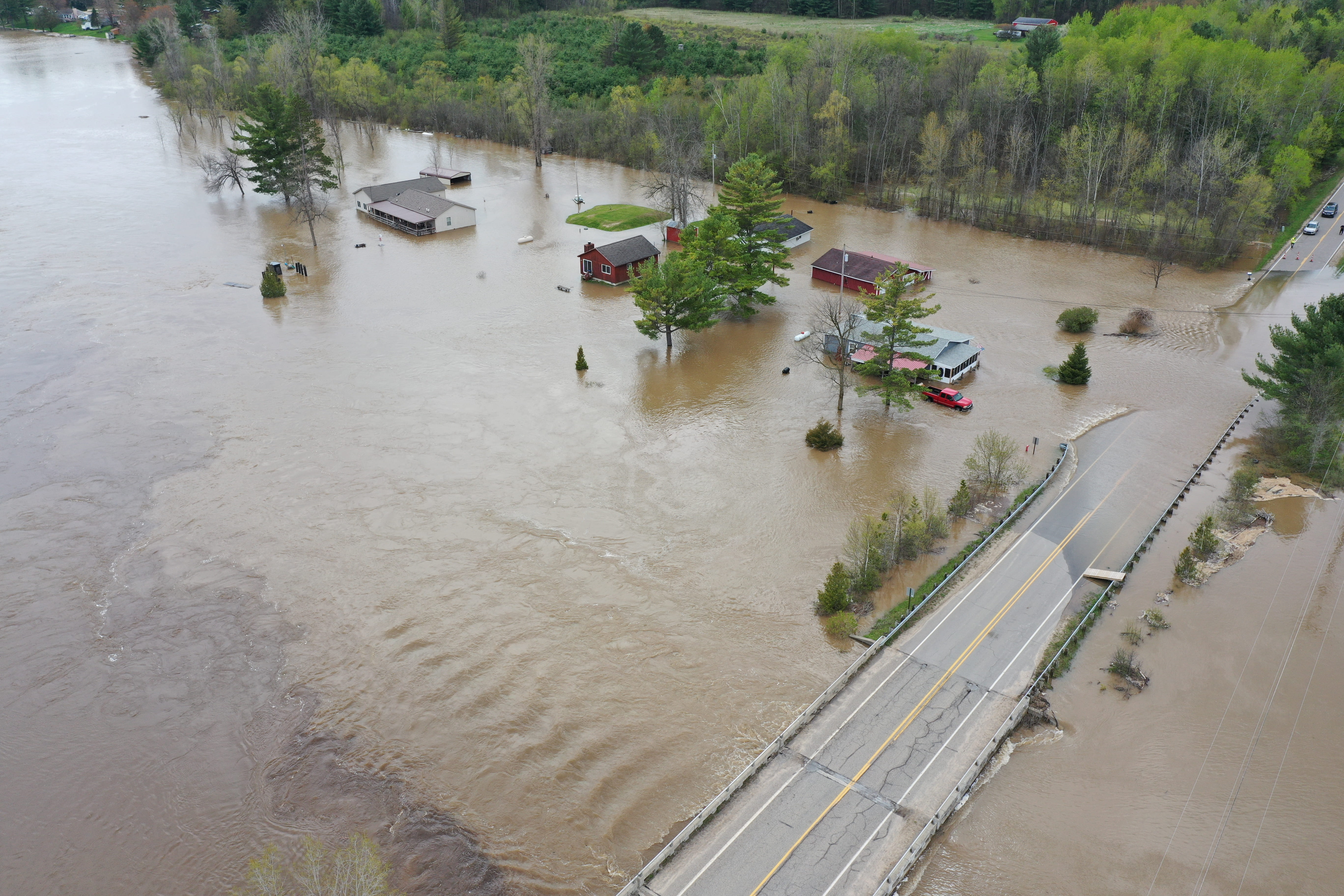 A road, buildings, and trees surrounded by flood water. 