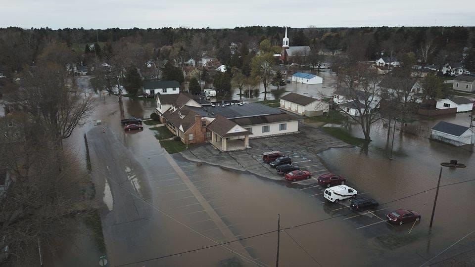 An aerial view of buildings and cars surrounded by flood water. 