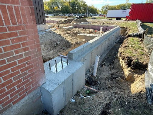 The foundation of a building with dug up dirt around it, next to a brick wall.