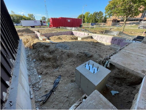 dug up dirt with a new building foundation next to the current building.