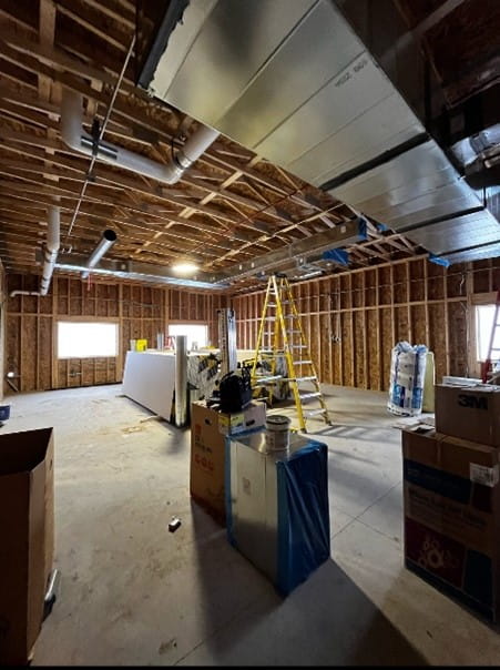 The inside of a building with exposed walls and ceiling and concrete floor. There is a ladder and building materials in the middle of the room. 