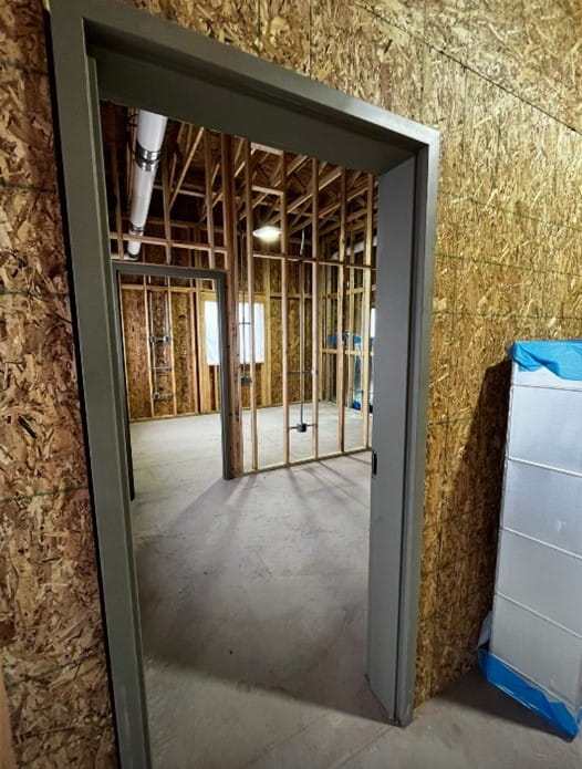 A view through a doorway into room with exposed walls and ceiling and concrete floor. 