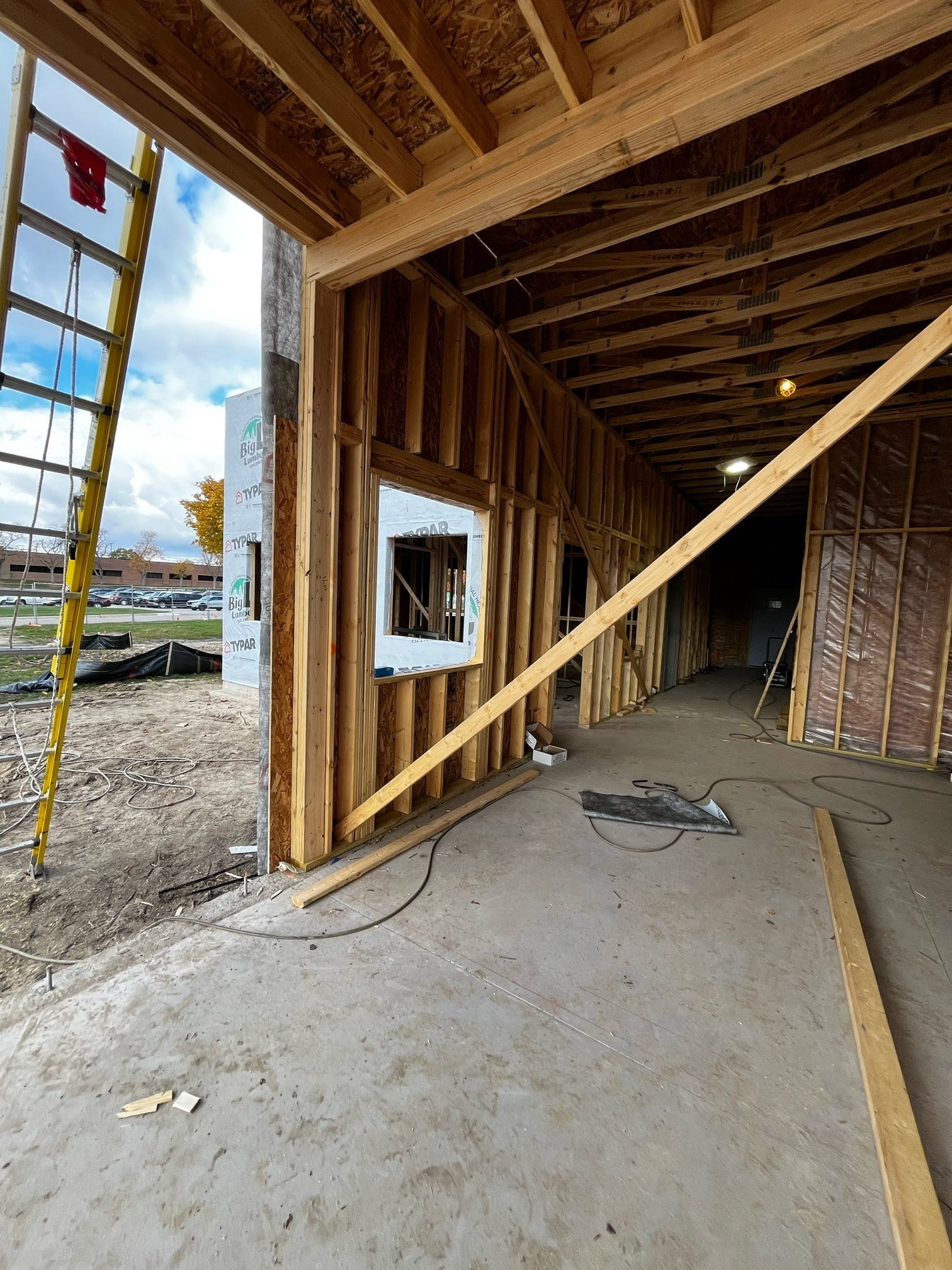 A room with exposed studs and a concrete floor and openings in the wall for windows an a door. 
