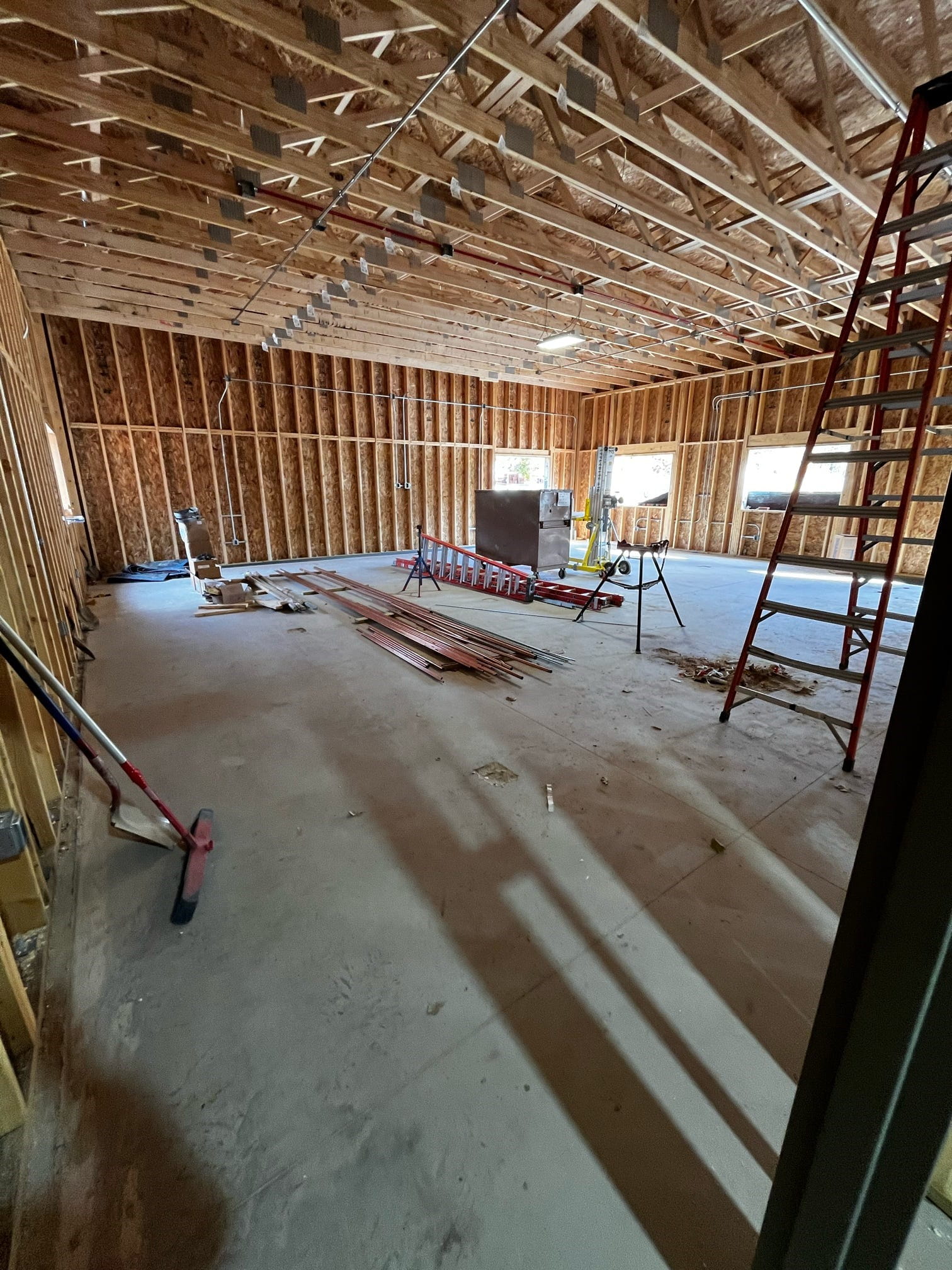 An unfinished room with exposed studs and a concrete floor, openings on the walls for windows and building supplies on the floor. 