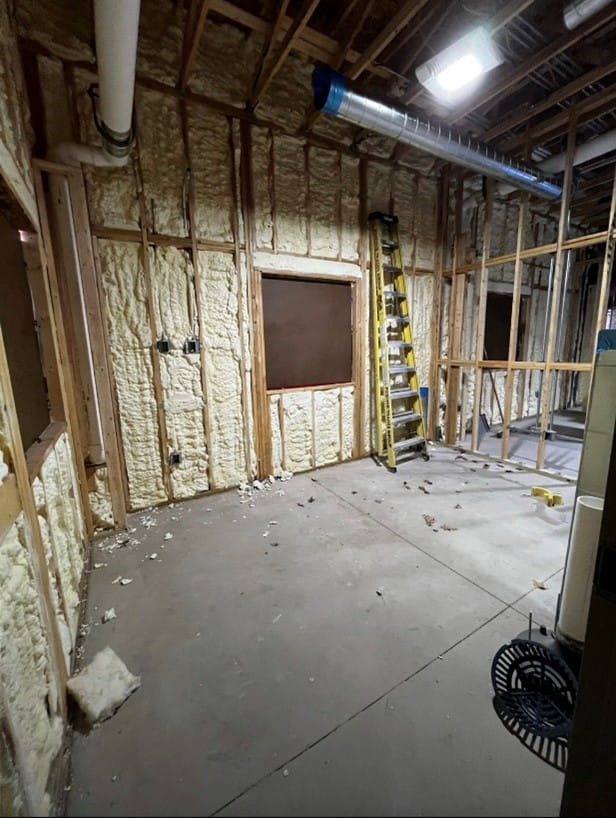 A room with exposed walls and ceiling and a concrete floor. There is insulation sprayed between the studs of the walls.